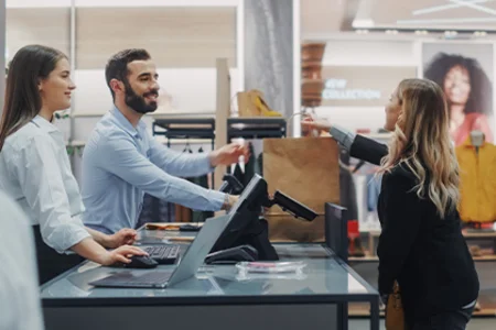 Retail – shopping with personal advice at the checkout Sales assistant hands shopping bag to customer in modern fashion store.